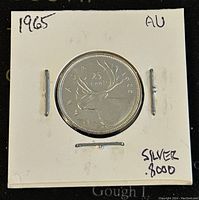 Reverse side of the 1965 Canadian 25 cent silver coin showing caribou design and inscriptions, in protective holder labeled with silver content and condition.