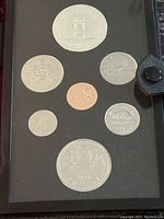 Photograph showing a set of Canadian coins including a large silver dollar coin at top and bottom with various smaller coins in between, arranged in a black album page.