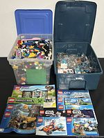 Two plastic bins filled with assorted Lego bricks and sealed bags along with LEGO instruction manuals laid out