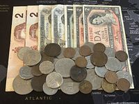 Full assortment of Canadian Banknotes and Coins showing multiple two dollar notes and an assortment of coins spread out on a world map background.