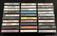 27 assorted music cassette tapes stacked showing front paper label covers with artist and album titles.