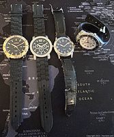 Four assorted wristwatches laid out on a map background, showing different styles and bands.
