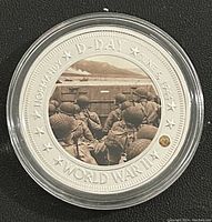 Obverse of the coin showing colored scene of soldiers in landing craft at Normandy beach with surrounding inscription.