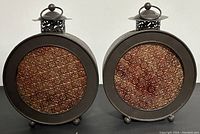 Pair of vintage metal circular candle holders with embossed copper-tone glass panels on front, showing entire front view of both pieces side by side.