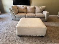 Beige three-seater couch with matching large square ottoman in a living room.