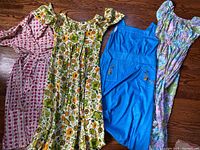 Four women's vintage dresses laid flat on wooden floor showing various colors and styles including floral prints, denim, and geometric pattern.