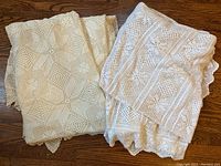 Two folded antique crochet bedspreads in cream color showing delicate crochet patterns and scalloped edges.