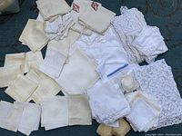 Full view of assortment of monogrammed antique linens and lace doilies laid out on floor, showing different sizes and embroidery.