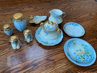 Full lot photo showing blue floral Bavarian porcelain dishes including plates, sugar bowl, creamer, and five art deco cobalt blue and gold salt and pepper shakers.