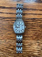 Full watch laid flat on wooden surface showing stainless steel bracelet, diamond bezel, and white dial with black numerals.