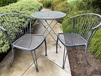 Full patio dining set for two with round collapsible table and two metal chairs, one with vertical slatted back and one with curved slatted back.