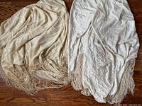 Two antique piano shawls laid together on wooden floor, showing color and fringed edges