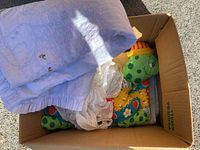 Box containing various baby items including embroidered white baby quilt, matching stuffed toy, and antique bonnets