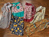 Overview of six colorful vintage aprons laid out on hardwood floor, showing different floral and paisley patterns