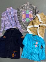 Overview photo showing all five sweaters and tops arranged flat, displaying colors and design features including knit textures and patchwork.