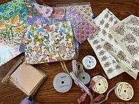 Overview photo showing multiple sheets of vintage wrapping papers with floral and butterfly patterns, along with spools of ribbons and craft stamp packets.