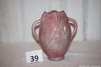 Front and side view of rose-colored pottery vase with stylized floral design and two handles.