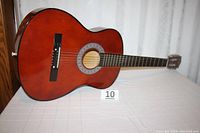 Full view of the reddish-brown acoustic classical guitar on a white cloth showing body shape and finish.