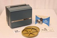 Bell and Howell projector inside original blue case with two film reels and two manuals placed on white surface