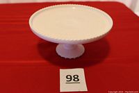 Side view of the pale pink milk glass cake stand with visible beaded edge and sturdy pedestal base.