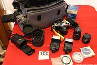 Camera bag, two flashes, three lenses, filters, manual, and camera body on a red surface.