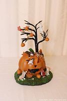Front view of Halloween tabletop tree with orange jack-o-lantern base, black tree with hanging pumpkins and Halloween figures, surrounded by playful kittens on grass base.