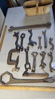 Full view of collection on a white table including a basket in the background and ruler for scale, showing many old wrenches and a clamp.