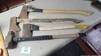 Full view of three axes and one sledgehammer laid out showing handles and heads