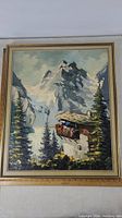 Full view of framed oil painting showing alpine mountain, chalet, and trees.