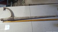 Full length photo showing the old logger's peavy with wooden handle and metal hook, placed next to a yardstick for length reference.