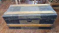 Front view of the old steamer trunk showing the patchwork worn panels, wooden slats, and metal reinforcements.