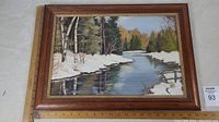Framed oil painting showing winter landscape scene with snow, trees, and river, includes measuring scale indicating 15.5 x 21.5 inches frame size