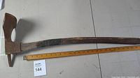 Full side view of the vintage adze showing the long wooden handle and rusted metal head alongside a ruler for length reference.
