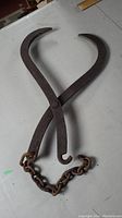 Full view of vintage forged metal ice block tongs with curved gripping arms and attached chain.