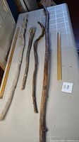 Four old walking sticks laid out on a table with measuring rulers showing their lengths