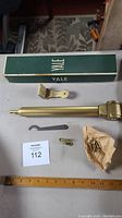 Photo showing Yale branded box, door closer arm, mounting bracket, wrench, and wrapped screws on table with ruler for scale.