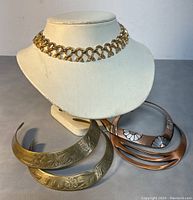 Set of five metal choker necklaces displayed on white neck forms and gray surface, showing overall lot condition and variety of designs.