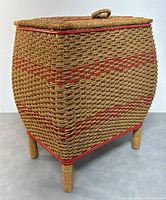 Front angled view of antique woven rattan sewing basket showing rectangular shape, woven lid with handle, and rattan legs.