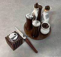 Art Deco cigarette lighter with wood base alongside Mid-Century Modern condiment set on wooden tray, including ceramic and wood containers and a small wood handled fork.