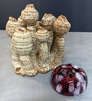 Photo showing abstract beige and brown pottery sculpture with multiple hollow columnar forms and a smaller spherical vessel with red and purple mottled glaze with multiple openings.