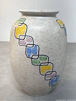 Front and side views of oval off-white speckled ceramic vase with colorful interlocking squares in hues of yellow, blue, green, mauve outlined in black.
