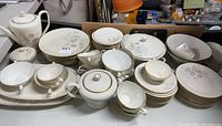 Full view of the entire dish set showing multiple stacked plates, bowls, teacups, saucers, covered pots and serving platters arranged on a table.