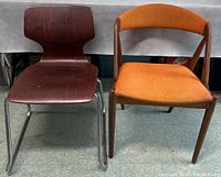 Two mid-century modern chairs side by side, a dark wood and metal sled base chair and an orange upholstered wooden chair.