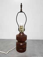 Side view of MCM teak bedside lamp unlit on grey surface.