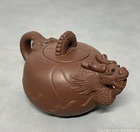 Angled close-up front view showing the dragon head spout with finely sculpted features and the lid with curled handle.