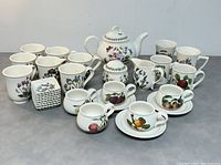 Full view of the lot showing the teapot with lid, sugar bowl with lid, creamer, multiple cups, small plates, and saucers arranged on a grey surface.