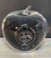 Front view of the clear glass apple paperweight showing engraved emblem including text and a lion figure.