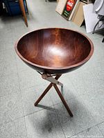 Wooden salad bowl displayed on the assembled wooden tripod stand, showing deep rounded shape and wood grain.