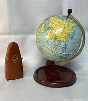 Side view of both the vintage tin world globe on stand and the brown Taktell Piccolo metronome
