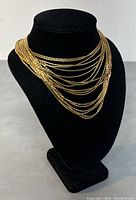 Front view of gold tone multi strand Monet necklace on black display stand.